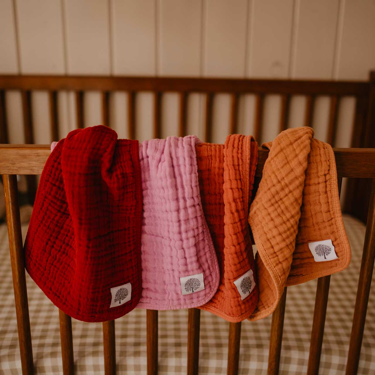 Four textured baby blankets in red, pink, orange, and brown hanging on a wooden chair.