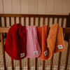 Four textured baby blankets in red, pink, orange, and brown hanging on a wooden chair.
