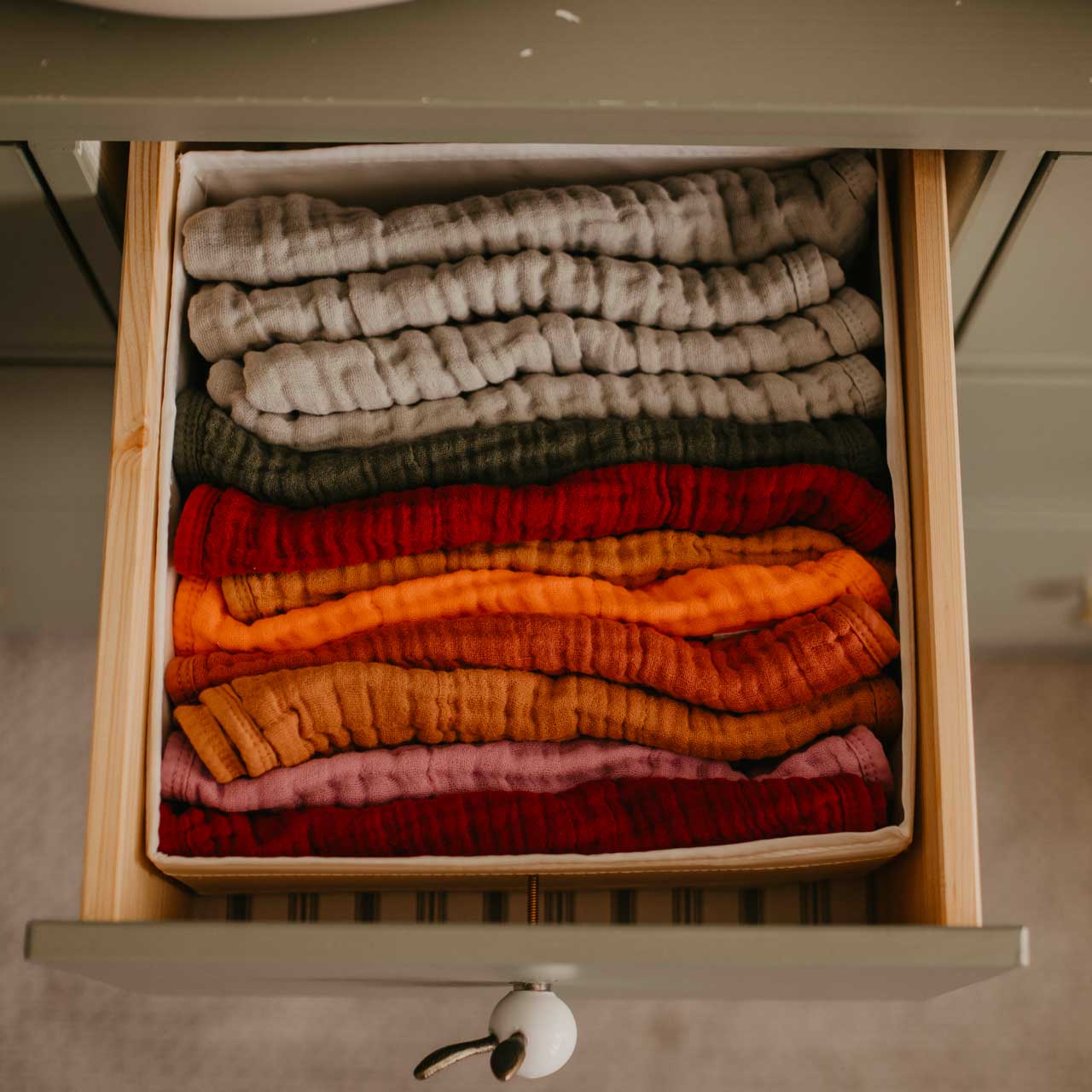 Folded sweaters in various colors arranged in a drawer.