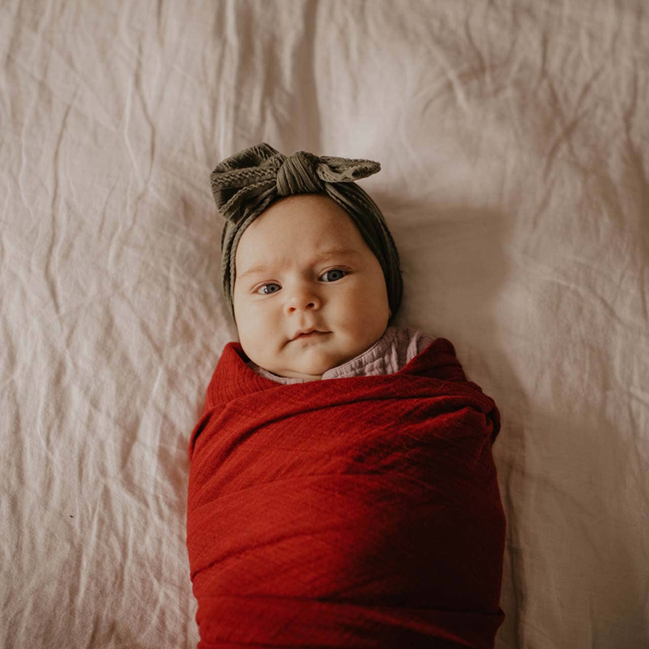 Newborn baby wrapped in red fabric with a headband on a soft beige background