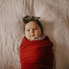Newborn baby wrapped in red fabric with a headband on a soft beige background