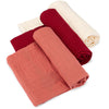 Three rolled-up fabric swaddles in red, terracotta, and cream on a white background