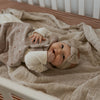 Baby lying on a soft blanket in a crib wearing a beige headband.