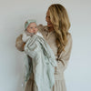 Woman holding a baby wrapped in a green blanket against a white background
