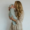 Woman holding a baby wrapped in a green swaddle against a white background