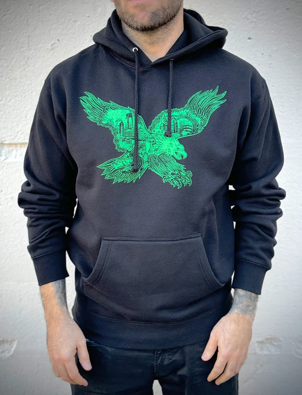 Person wearing a dark hoodie with a green eagle design on a plain background