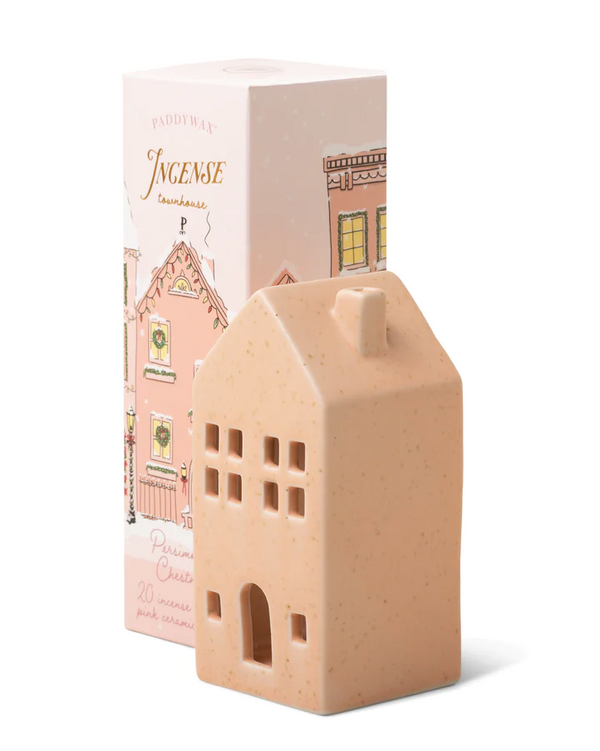 A beige ceramic incense cone holder shaped like a townhouse, with a pink Christmas-themed box in the background.