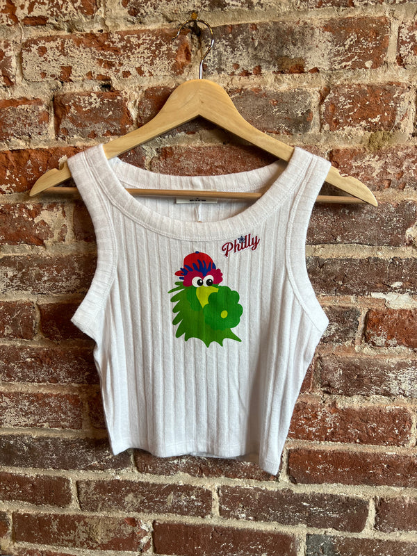 White tank top with a colorful parrot design and 'Pittily' text on a wooden hanger against a brick wall.