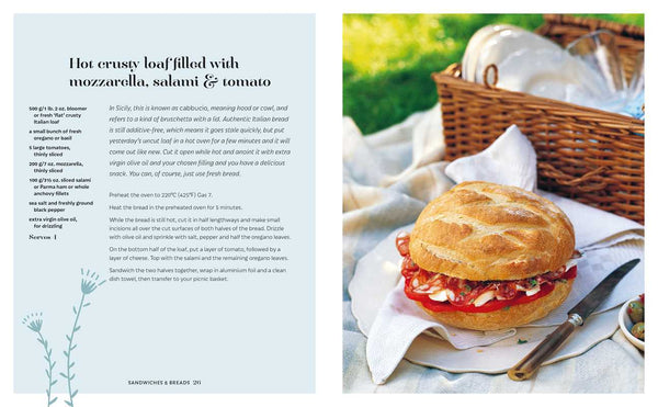 Sandwich with mozzarella, salami, and tomato on a picnic setting with a basket and cutlery.