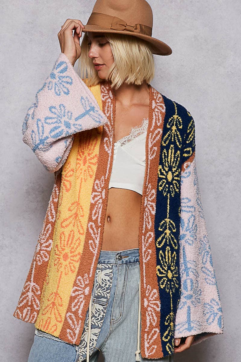 Person wearing a colorful patterned cardigan over a white top and jeans, holding a pink and blue patterned towel.