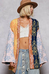 Woman wearing a colorful patterned cardigan over a white top and blue jeans, with a brown hat.