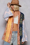 Person wearing a colorful patterned cardigan over a white top and jeans, holding a pink and blue patterned towel.