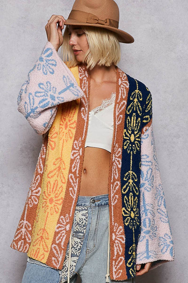 Person wearing a colorful patterned cardigan over a white top and jeans, holding a pink and blue patterned towel.