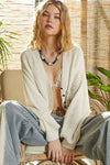 Woman sitting in a chair wearing a white cardigan and pants with a woven background
