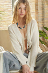 Woman wearing a white cardigan over a sheer top with a blurred background