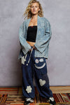 Woman wearing a denim jacket and blue pants with patches against a gray background