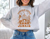 A woman wearing a gray sweatshirt with 'PUMPKIN PATCH JUNKIE' text and a pumpkin patch design.