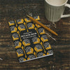 Notebook with yellow floral pattern and text on a wooden surface with a mug and pen.