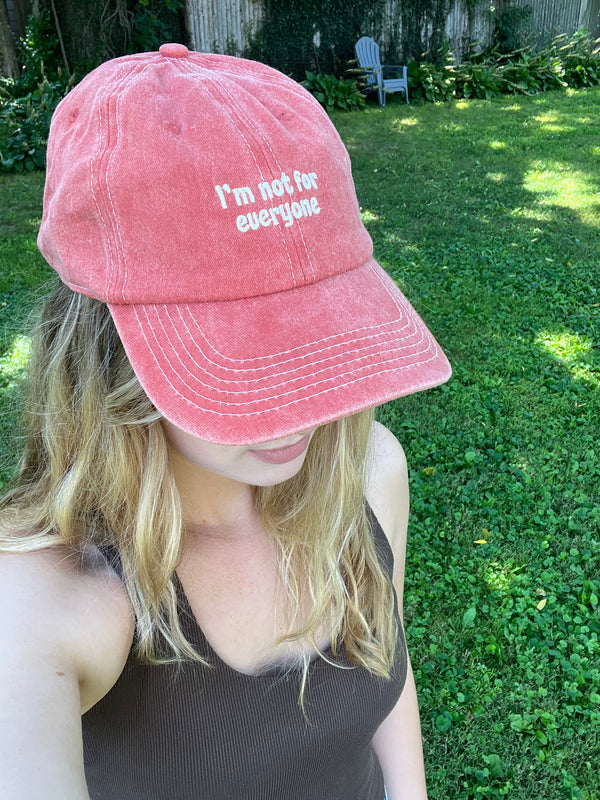 Person wearing a pink cap with 'I'm not for everyone' text outdoors.
