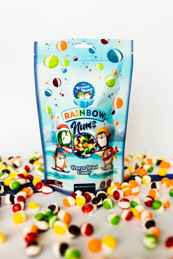 A bag of Rainbow Nums freeze-dried candy displayed with scattered candy pieces in the foreground.