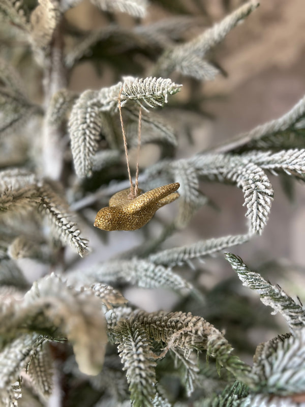 A gold-finished resin bird ornament hanging on a festive Christmas tree.