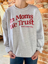 Person wearing a gray sweatshirt with red text 'In Moms We Trust' against a brick wall.