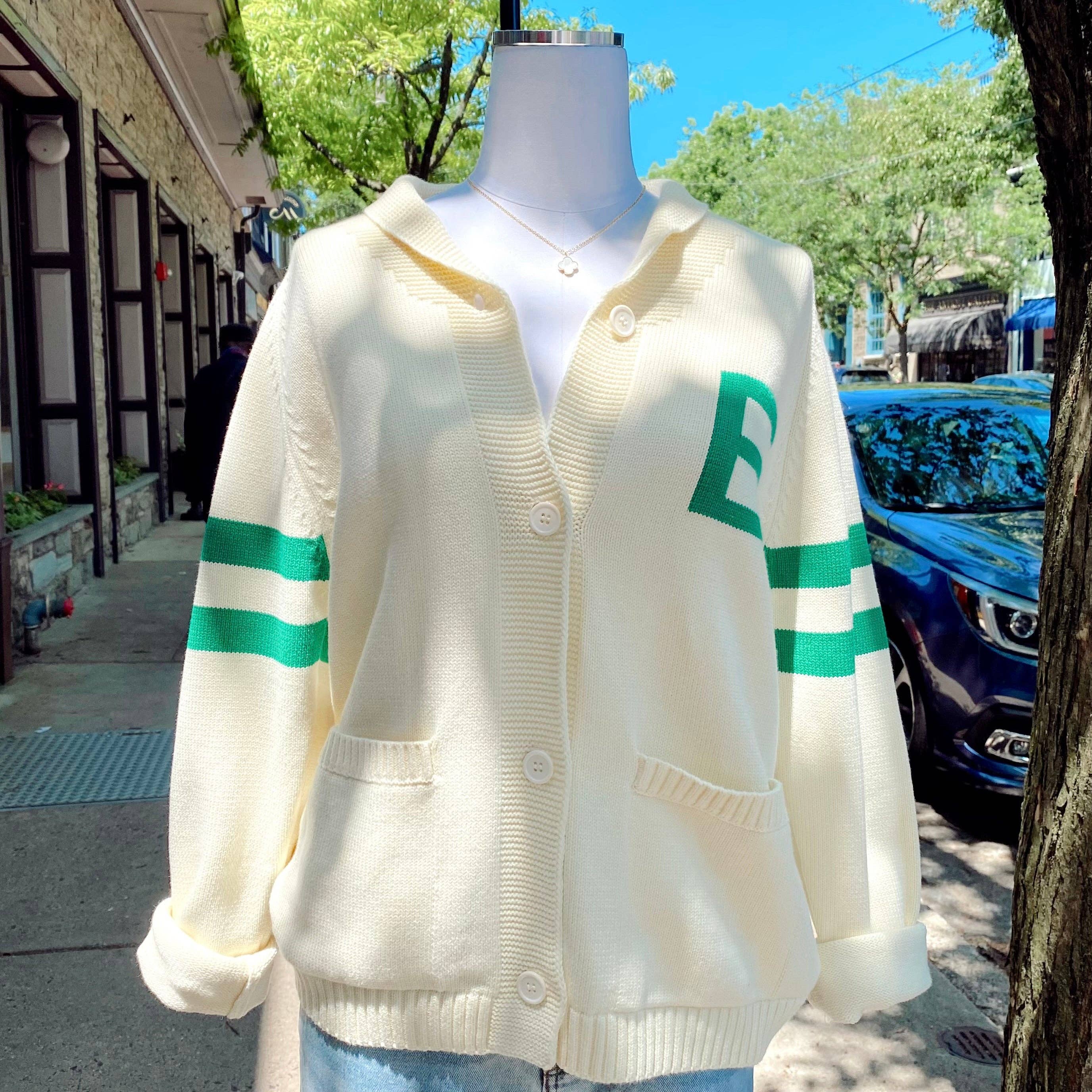 A beige and green striped cardigan with the letter 'E' on the front and 'Go Birds' on the back, displayed on a mannequin outdoors.