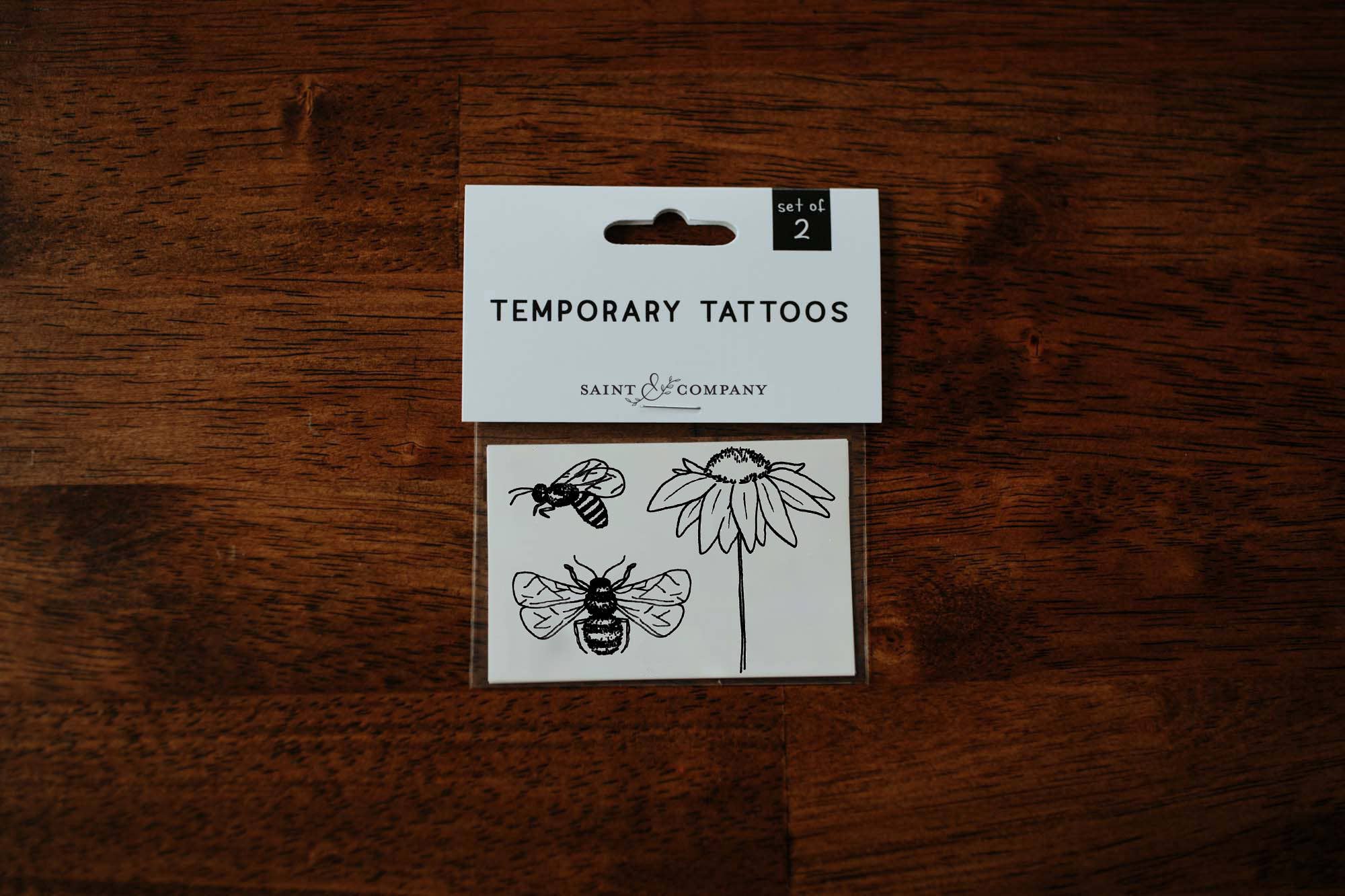 A pack of temporary tattoos featuring a coneflower and honeybees, placed on a wooden surface.