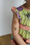 Child's arm with temporary tattoos wearing a colorful floral dress.