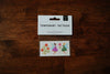 A pack of temporary tattoos featuring two fairies with fairy dust and orange flowers, presented on a wooden surface.