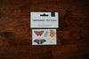 A pack of 'Secret Garden' temporary tattoos featuring hand-painted butterflies, flowers, and greenery, placed on a wooden surface.