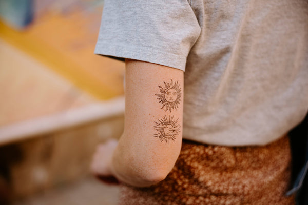 A person is showing off a temporary tattoo of two sun designs on their forearm.