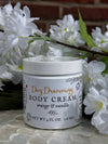 Jar of Day Dreaming Body Cream with white flowers in the background