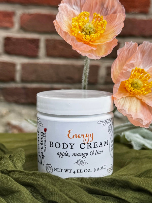Body cream jar labeled 'Energy' with flowers in the background