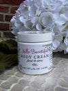 Jar of body cream with floral design on a textured surface with white flowers in the background.