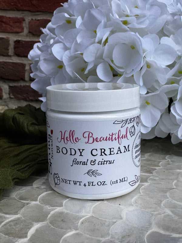 Jar of body cream with floral design on a textured surface with white flowers in the background.