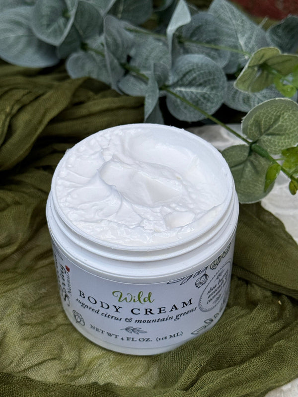 Jar of Wild Body Cream on a green fabric background with plants.