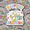 Colorful sticker with a cartoon character and text 'Happiest when I'm Reading' on a patterned background.