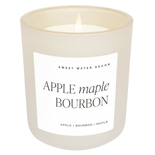 A beige candle labeled 'APPLE MAPLE BOURBON' with 'Sweet Water Decor' on the label, indicating a scent blend of apple, maple, and bourbon with a hint of cinnamon and coconut.