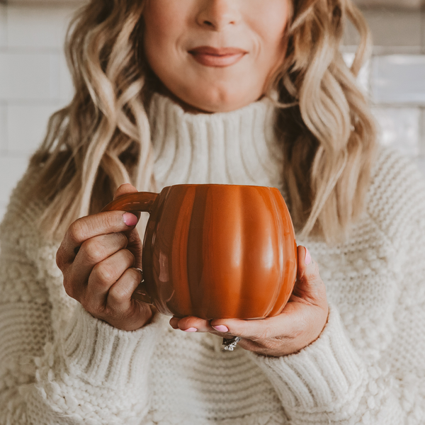 Woman holding a pumpkin mug in a cozy setting