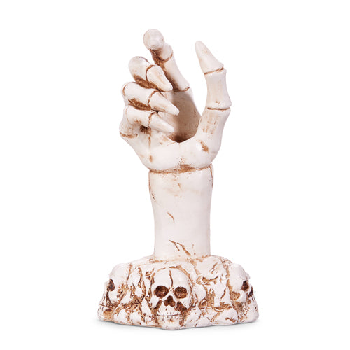 A beige candle holder in the shape of a hand with a skeleton design and a skull at the base.