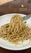 Spaghetti on a white plate with a fork, garnished with herbs, on a wooden table.