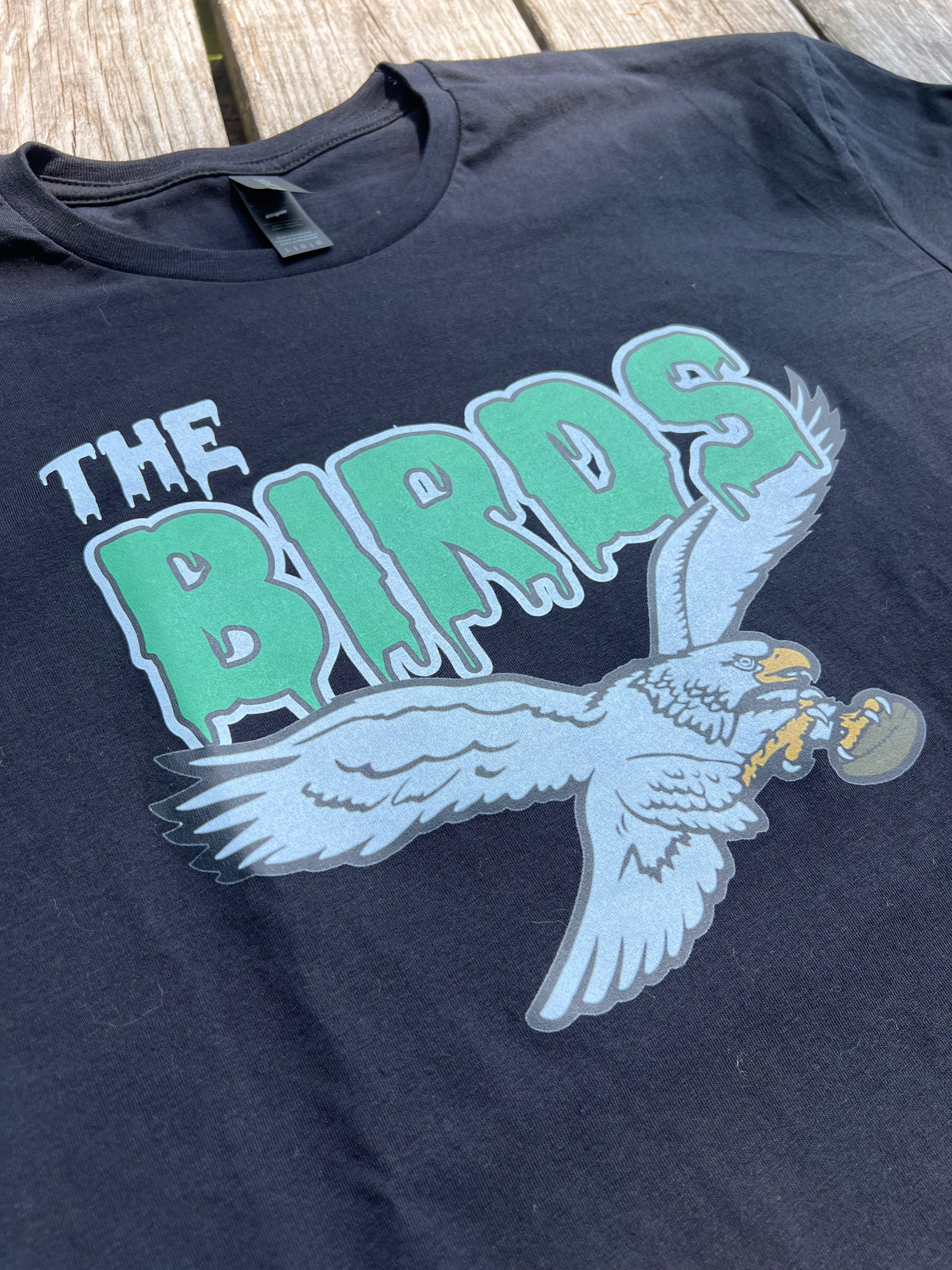 Black t-shirt with 'The Birds' graphic design featuring a parrot on a wooden surface.