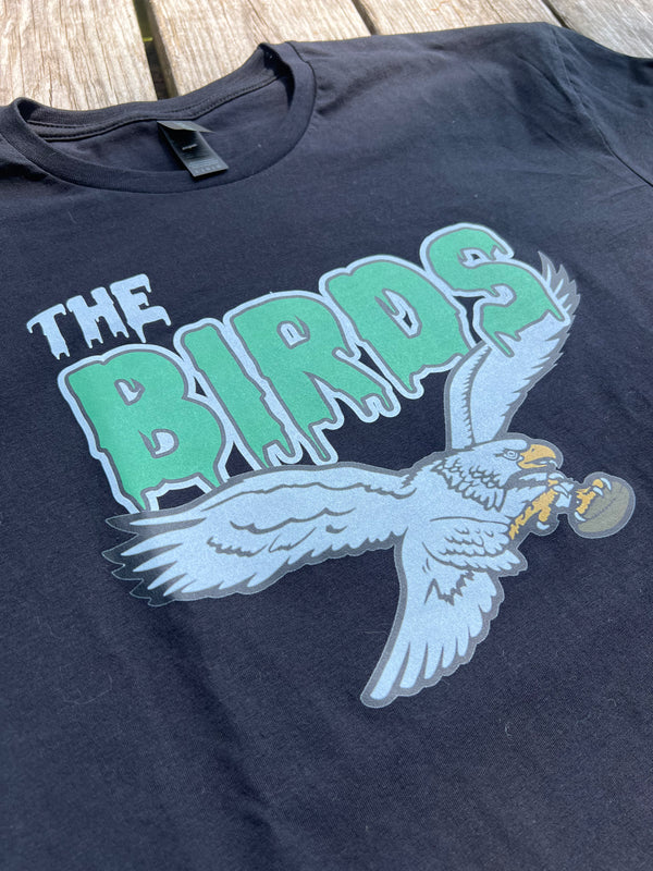 Black t-shirt with 'The Birds' graphic design featuring a parrot on a wooden surface.
