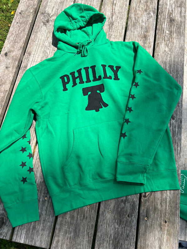 Green hoodie with 'PHILLY' and bell graphic on a wooden surface