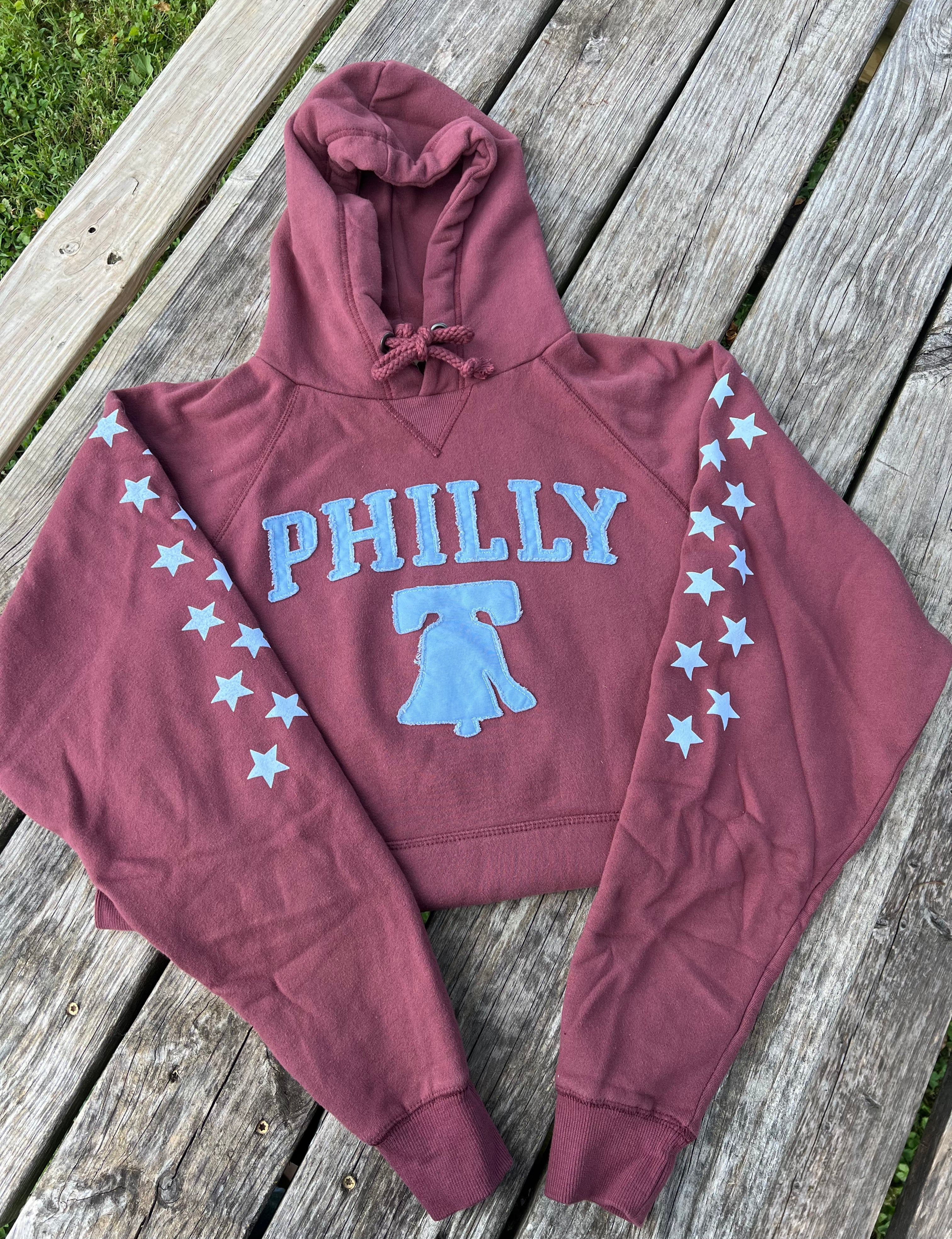 Maroon hoodie with 'PHILLY' and Liberty Bell design on a wooden surface