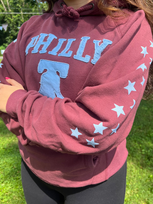 Maroon hoodie with 'PHILLY' and star designs, worn outdoors.