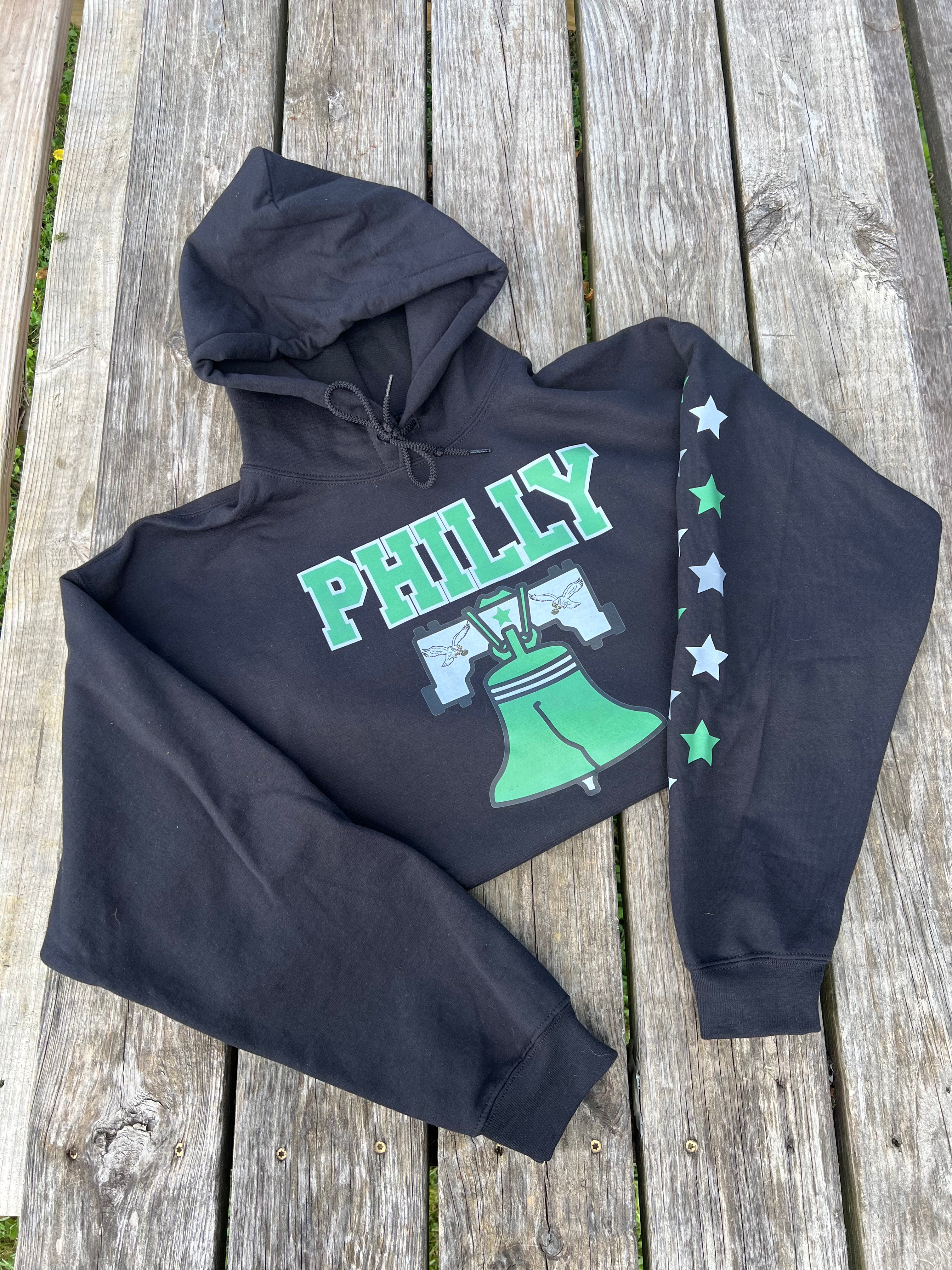 Black hoodie with 'PHILLY' and Liberty Bell design on a wooden surface