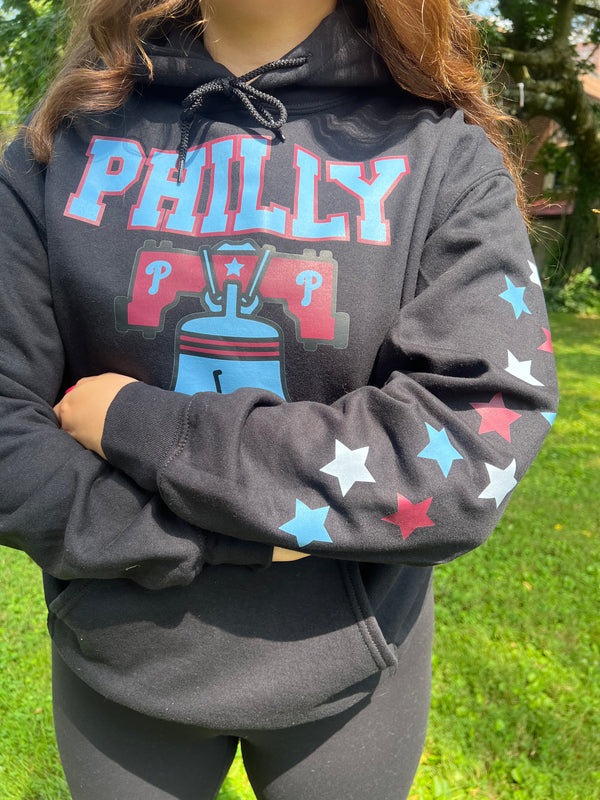 Person wearing a black hoodie with 'PHILLY' and star designs outdoors.