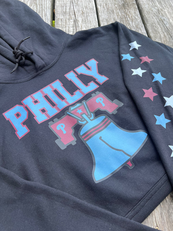 Black hoodie with 'PHILLY' and Liberty Bell graphic on a wooden surface